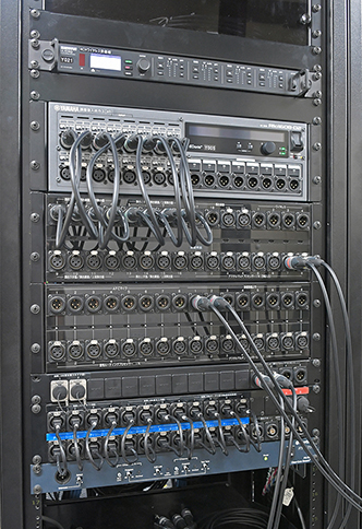 最適な環境を維持するアンプ室に整然と並ぶ機器架群。写真左＝「SHURE」の4chワイヤレス受信機「ULXD4Q」、「ヤマハ」のI/Oラック「Rio1608-D2」、さまざまな入出力がスムーズに行なえるよう考えられたパッチ盤などが収納されたラック。写真中＝デジタルマルチプロセッサー「MRX7-D」、「AFC3」システムおよび残響付加プロセッサー「LAP3-AFC」、メインスピーカーを駆動する「NEXO NXAMP4×2　MK2」パワーアンプが収納されたラック。写真右＝サラウンドスピーカー用のパワーアンプ「ヤマハPX8」